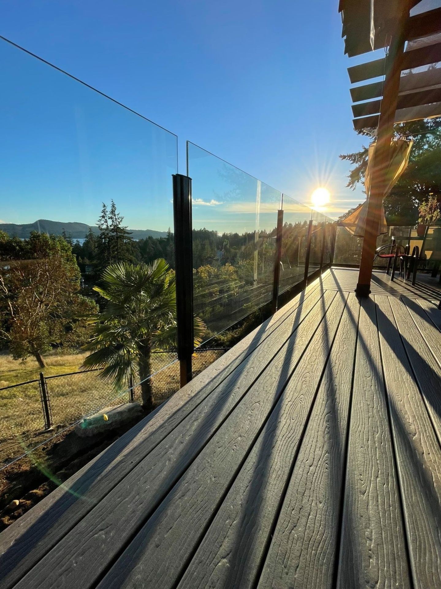Gray composite deck with glass railings casting shadows across the deck.