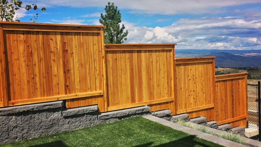Cedar fence going down a terraced hillside with views of a cloudy sky and surrounding landscape.